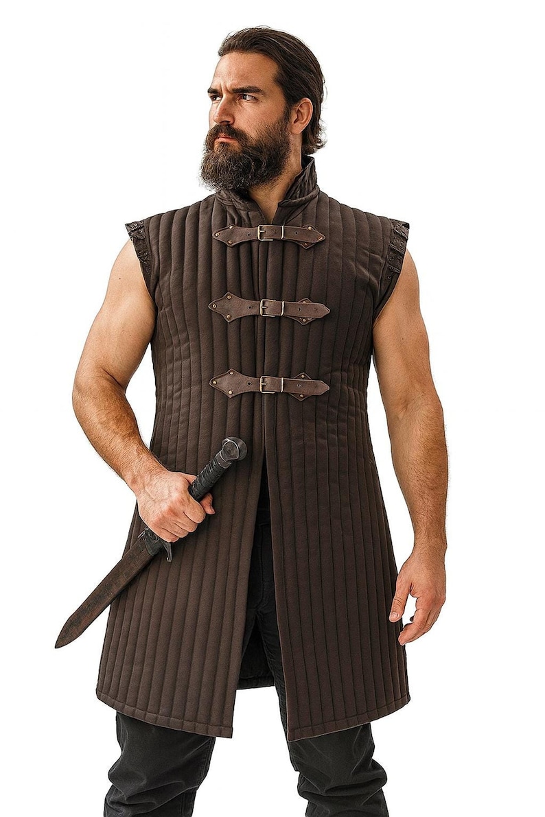 A bearded man wearing a brown sleeveless quilted gambeson and holding a dagger against a white background.