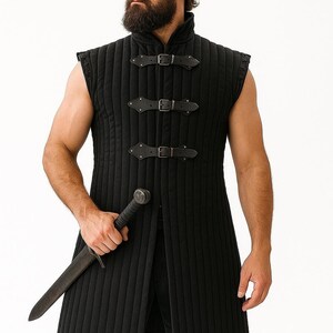 A bearded man wearing a black sleeveless quilted gambeson holding a dagger against a plain white background.