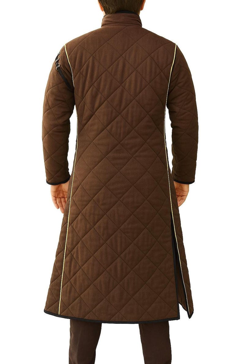 The back view of a person wearing a long brown quilted gambeson coat with yellow piping along the seams.