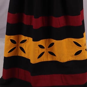 Pode incluir: Saia longa com listras horizontais em preto, bord&ocirc; e dourado. A se&ccedil;&atilde;o dourada apresenta desenhos florais recortados. A saia parece ser feita de um tecido macio e fluido.