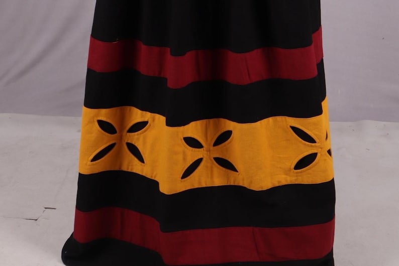 Pode incluir: Saia longa com listras horizontais em preto, bord&ocirc; e dourado. A se&ccedil;&atilde;o dourada apresenta desenhos florais recortados. A saia parece ser feita de um tecido macio e fluido.