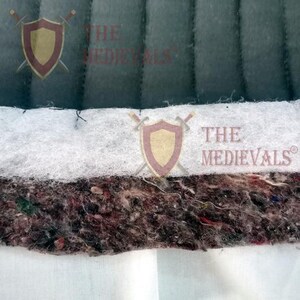 A close-up cross-section view showing the layers of quilted fabric material, including dark green fabric, white batting, and a thick speckled inner padding layer.