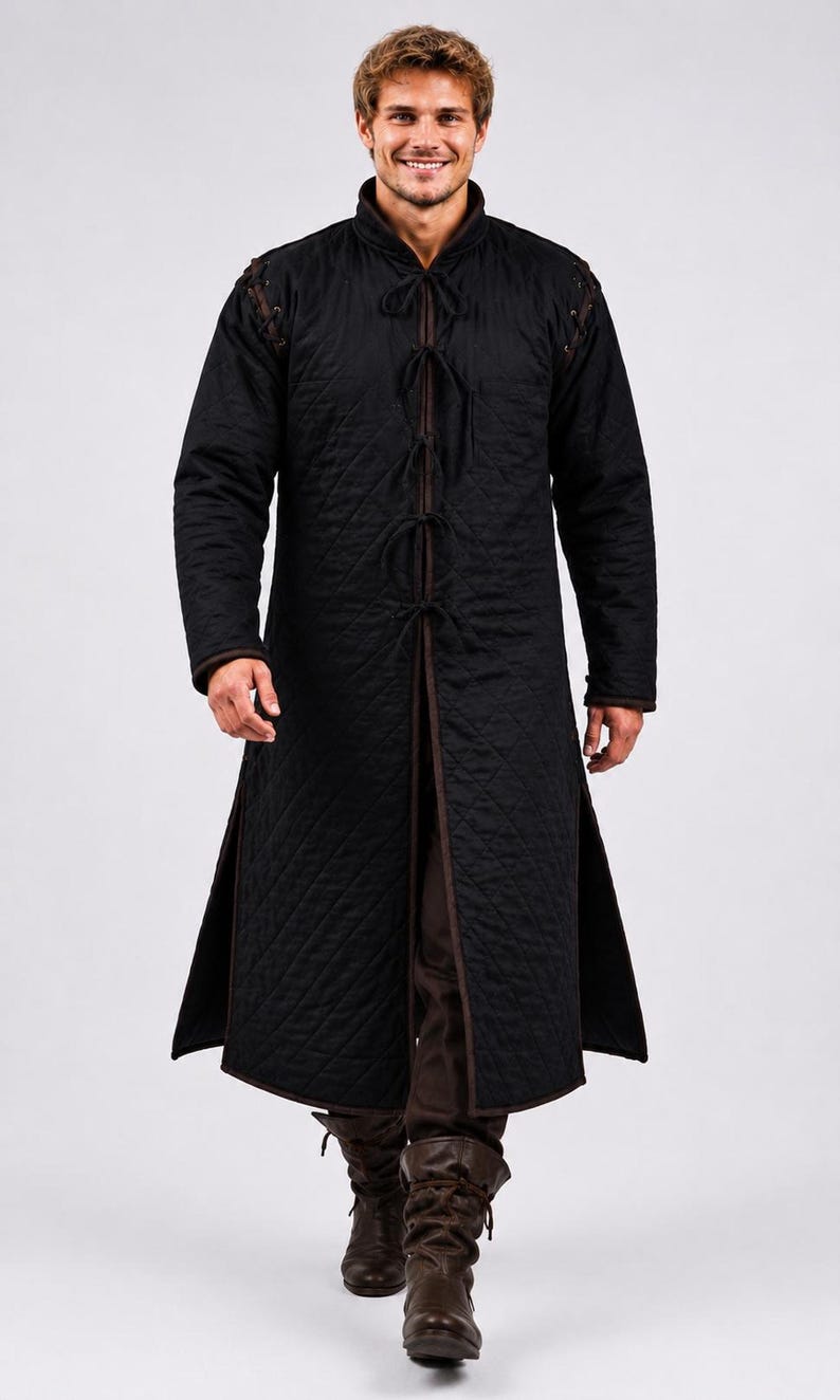 A man wearing a black quilted long gambeson coat walking forward toward the camera.