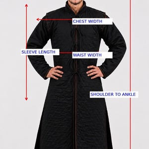 A diagram over the black gambeson coat showing measurement lines and labels for chest width, waist width, sleeve length, and shoulder to ankle.