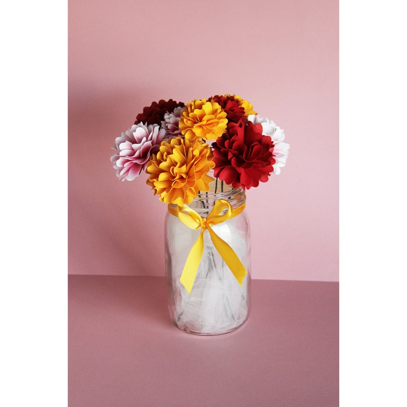 May include: A bouquet of paper flowers in shades of red, yellow, and white arranged in a clear glass jar with a yellow ribbon tied around the neck.