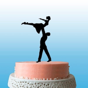 May include: A black silhouette of a couple dancing on a two-tiered cake. The woman is being lifted by the man. The cake is decorated with white pearls around the bottom tier.