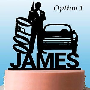 Könnte beinhalten: Ein schwarzer Tortenstecker mit der Silhouette eines Mannes im Anzug, der eine Waffe hält, einem Oldtimer, dem Text 007 und dem Namen JAMES. Der Text Option 1 ist oben rechts sichtbar. Der Tortenstecker steht auf einem hellrosa Kuchen.