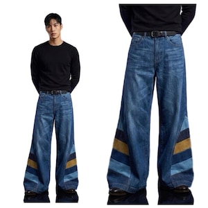 Könnte beinhalten: Weit geschnittene blaue Jeans aus Denim mit hoher Taille und schwarzem Gürtel. Die unteren Hosenbeine zeigen diagonale, farblich abgesetzte Einsätze in Hellblau, Dunkelblau und Senfgelb, die ein markantes Streifenmuster erzeugen.