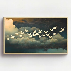 Könnte beinhalten: Ein gerahmtes Kunstwerk zeigt einen Schwarm weißer Vögel im Flug vor dem Hintergrund dunkler, dramatischer Wolken und eines goldenen Himmels. Die Vögel sind mit detaillierten Flügeln gemalt, was ein Gefühl von Bewegung und Freiheit erzeugt. Das Kunstwerk ist in einem hellen Holzrahmen gerahmt.