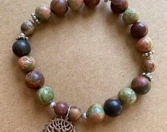 Op de afbeelding: Een armband gemaakt van bruine, groene en zwarte stenen met zilveren accenten. De armband heeft een levensboombedel.