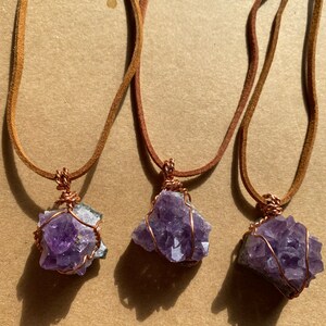 May include: Three amethyst crystal necklaces with copper wire wrapping. Each necklace has a brown leather cord.