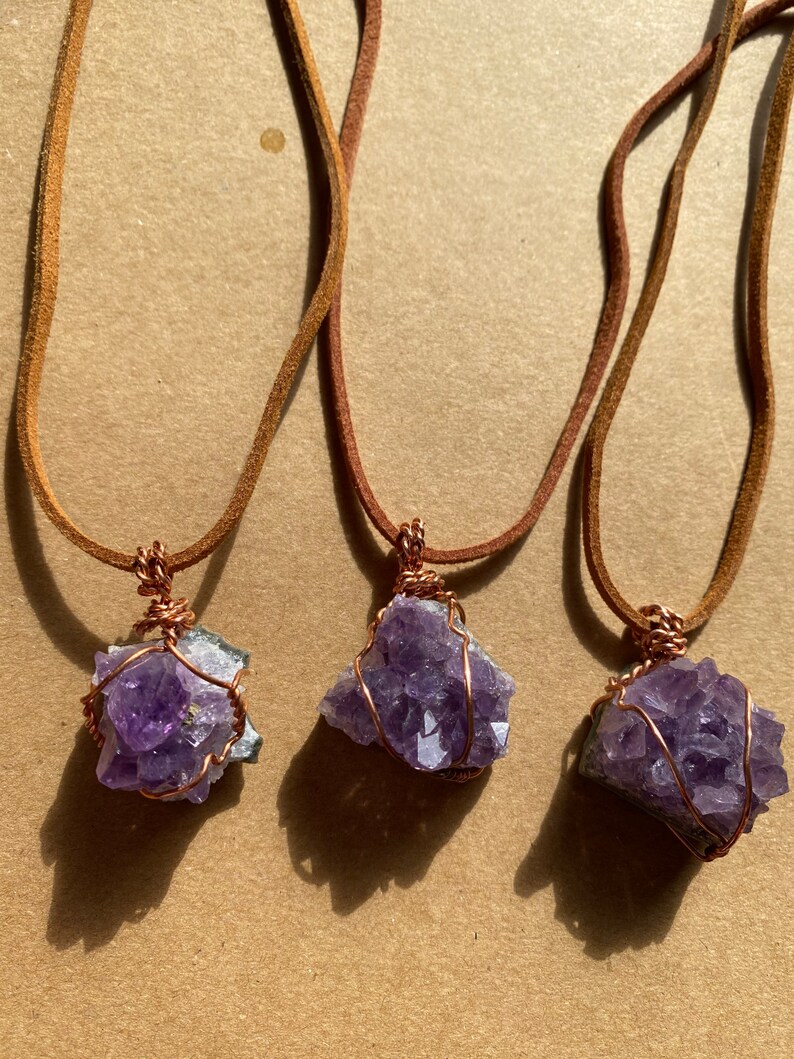 May include: Three amethyst crystal necklaces with copper wire wrapping. Each necklace has a brown leather cord.
