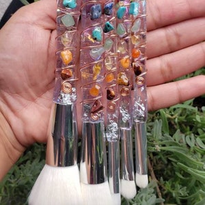 May include: Set of five makeup brushes with clear handles wrapped in copper wire and adorned with colourful gemstones. The brushes have white bristles and silver metal ferrules.