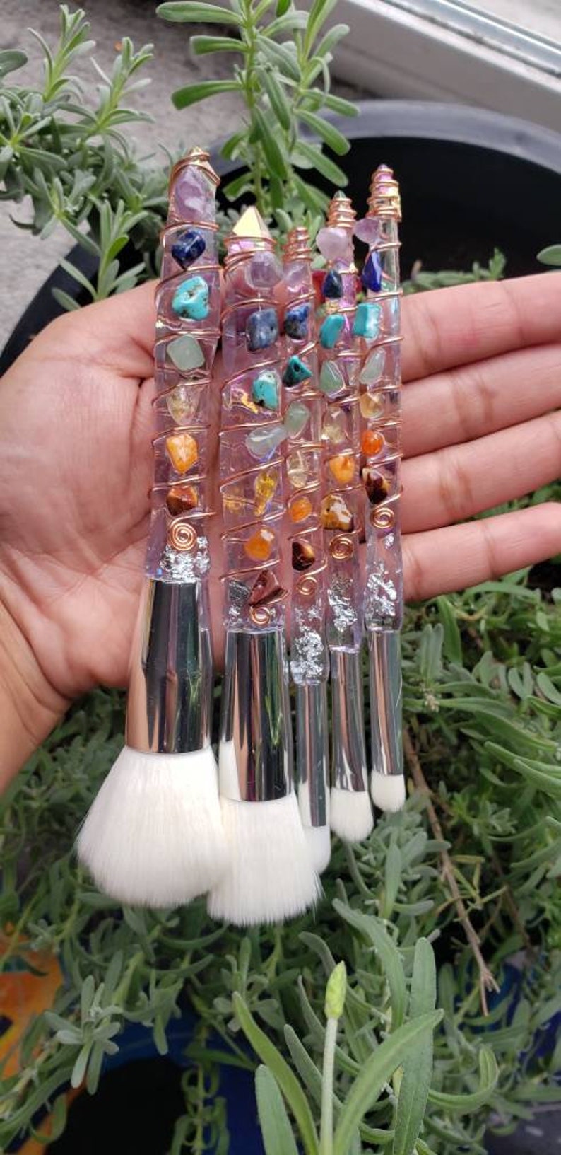 May include: Set of five makeup brushes with clear handles wrapped in copper wire and adorned with colourful gemstones. The brushes have white bristles and silver metal ferrules.