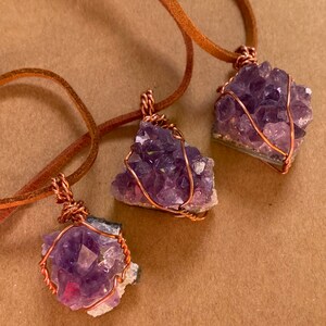 May include: Three amethyst crystal pendants wrapped in copper wire and hanging from brown leather cords.