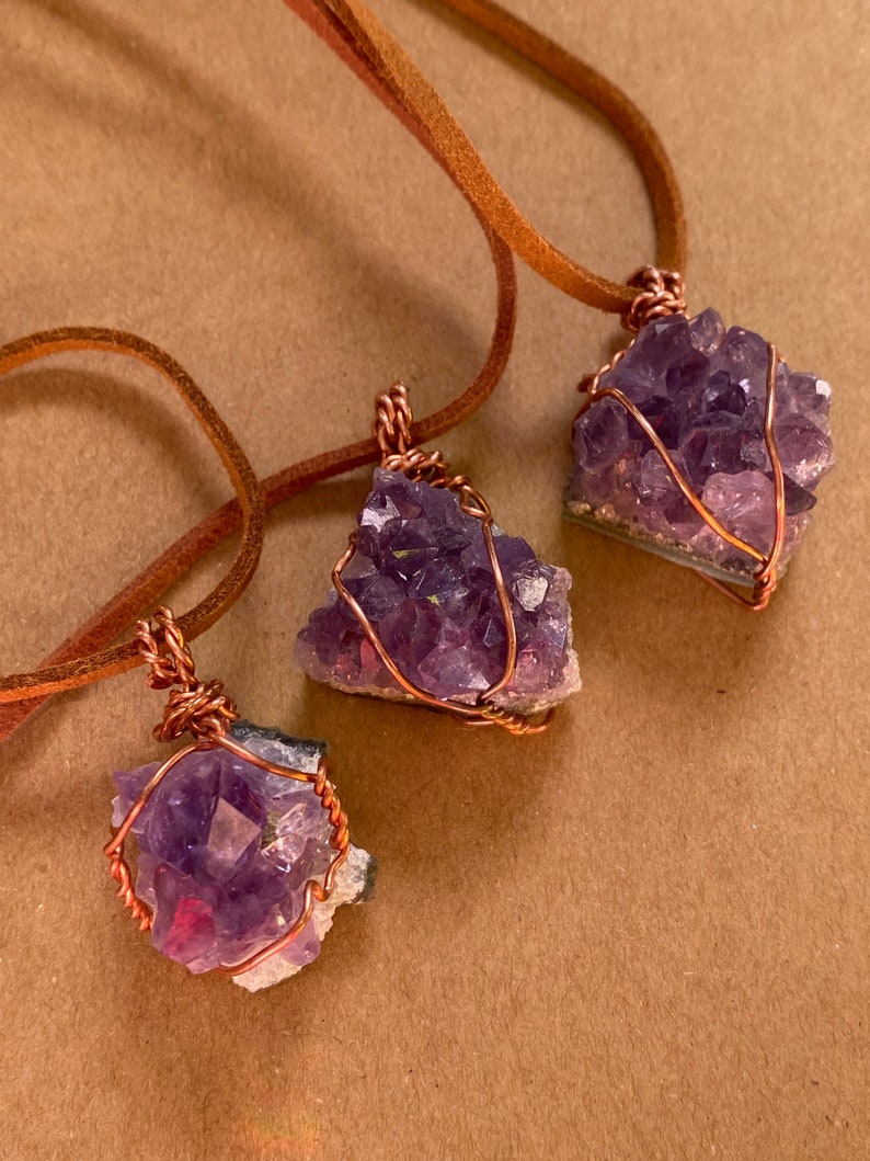 May include: Three amethyst crystal pendants wrapped in copper wire and hanging from brown leather cords.