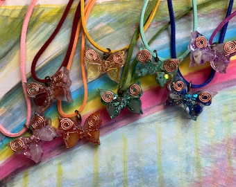 May include: A collection of eight butterfly necklaces with different colored resin and crystal accents. Each necklace features a copper wire butterfly with a spiral design. The necklaces are displayed on a colorful background.