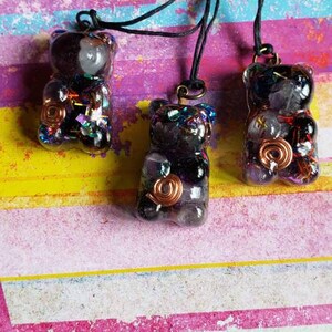May include: Three resin bear pendants with a black and purple color scheme. Each pendant is filled with various crystals and a copper wire spiral. The pendants are hanging from black cords.