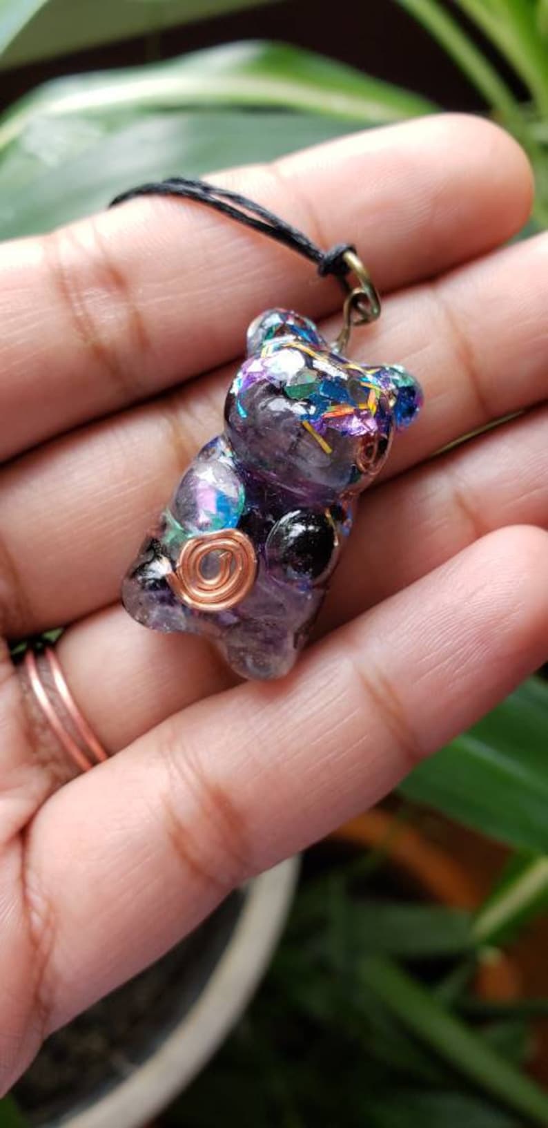 May include: A purple and black resin bear charm with iridescent glitter and copper wire accents. The charm is attached to a black cord.