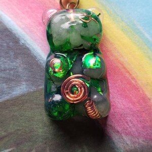 Op de afbeelding: Een ketting met een groene gummy bear hanger met koperen draadaccenten. De hanger is gemaakt van helder hars met groene glitter en koperen draadaccenten. De ketting is aan een zwart koord.