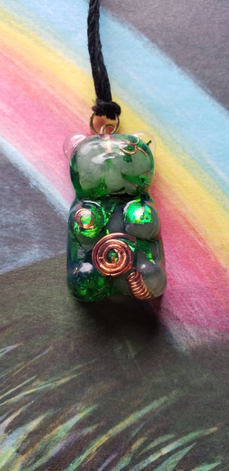 Op de afbeelding: Een ketting met een groene gummy bear hanger met koperen draadaccenten. De hanger is gemaakt van helder hars met groene glitter en koperen draadaccenten. De ketting is aan een zwart koord.