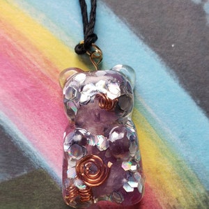 Op de afbeelding: Een paarse en zilveren glitterhars gummy bear hanger met koperen draadaccenten, hangend aan een zwart koord.