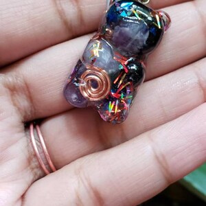 May include: A resin bear charm necklace with a copper wire wrapped around a purple amethyst stone. The bear is filled with iridescent glitter and black and blue stones.