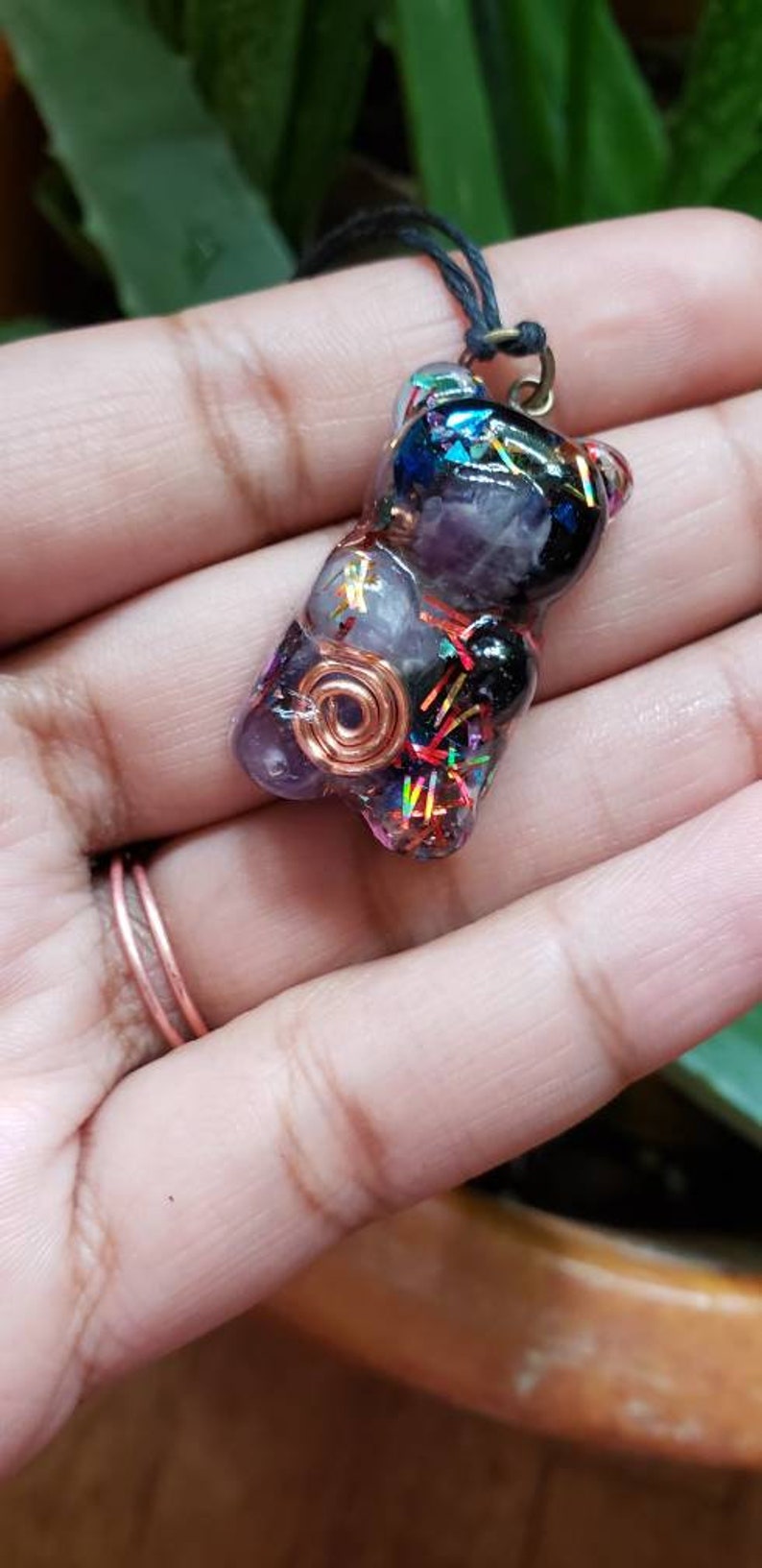 May include: A resin bear charm necklace with a copper wire wrapped around a purple amethyst stone. The bear is filled with iridescent glitter and black and blue stones.