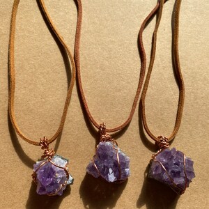May include: Three amethyst crystal necklaces with copper wire wrapping. Each necklace has a brown leather cord.