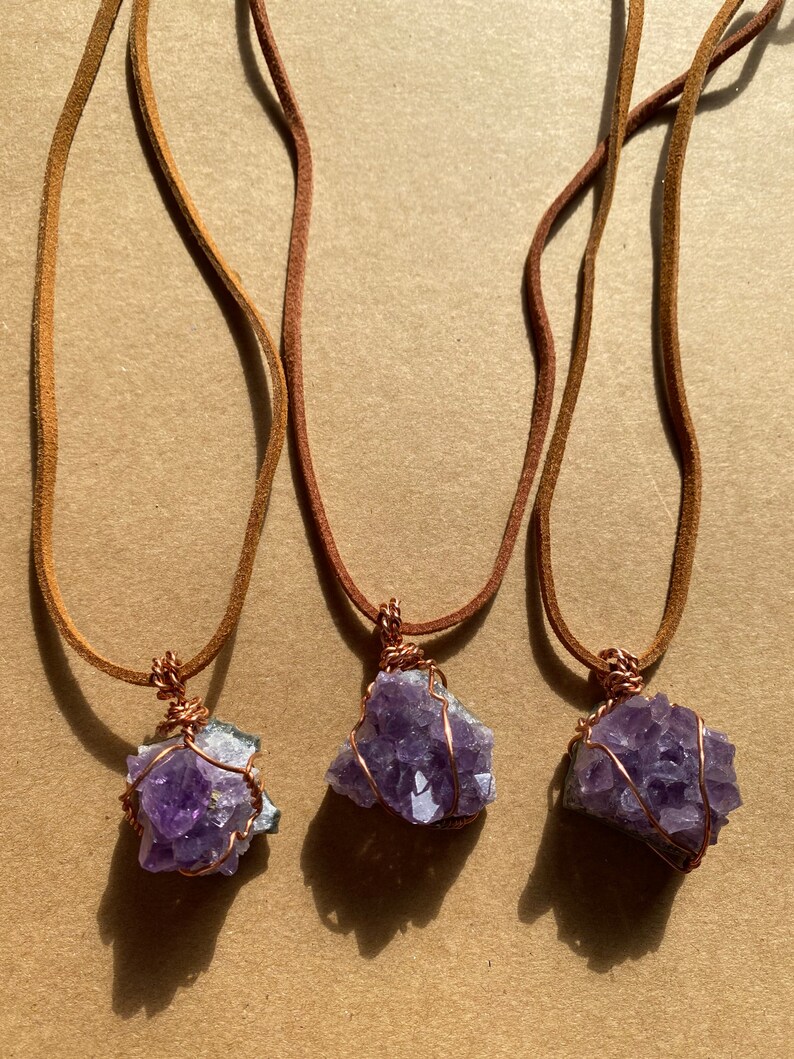 May include: Three amethyst crystal necklaces with copper wire wrapping. Each necklace has a brown leather cord.