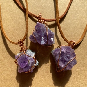 May include: Three amethyst crystal pendants wrapped in copper wire and hanging from brown leather cords.