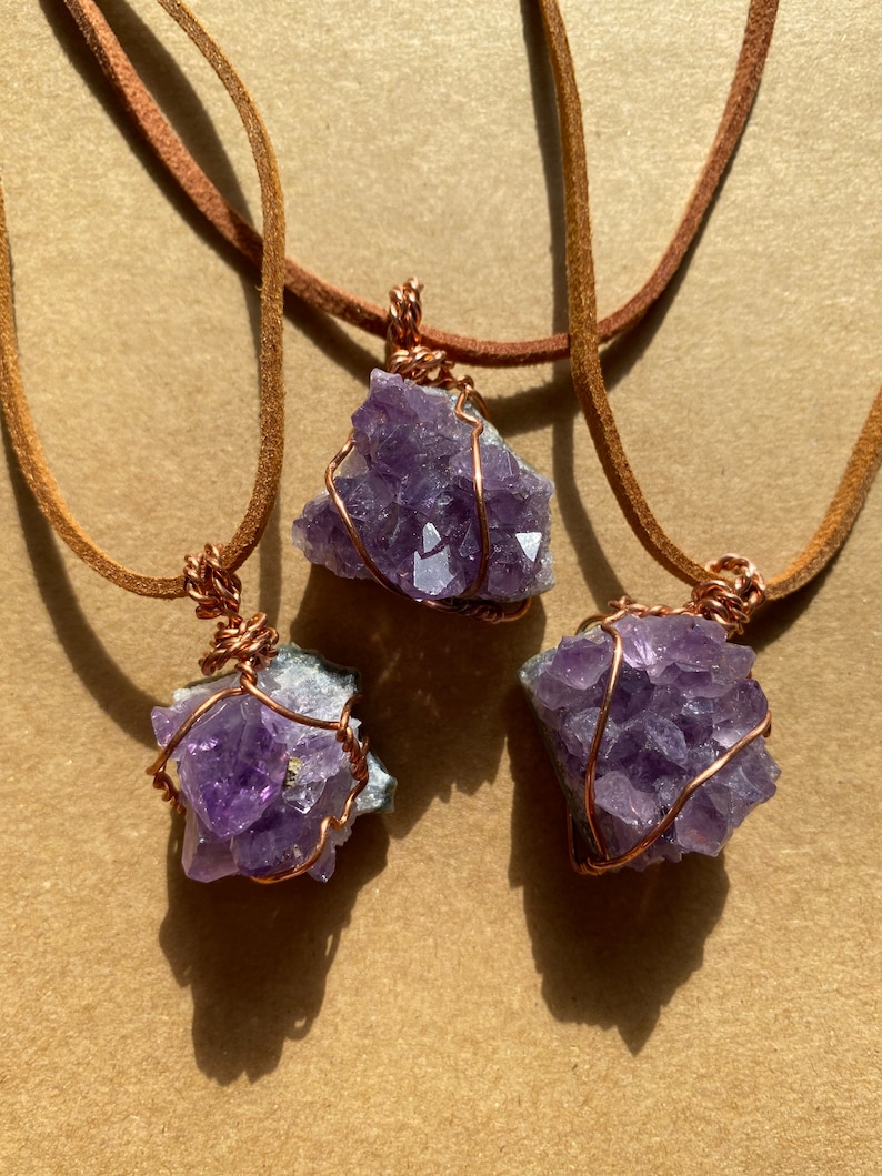 May include: Three amethyst crystal pendants wrapped in copper wire and hanging from brown leather cords.