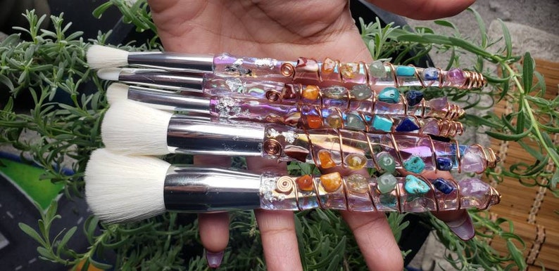 May include: Set of five makeup brushes with clear handles wrapped in copper wire and various colourful gemstones. The brushes have white bristles and silver metal ferrules.
