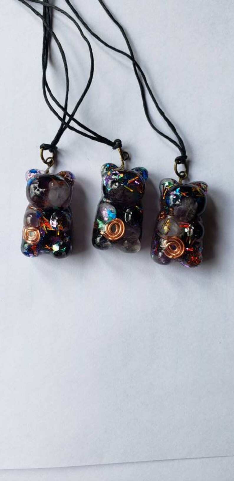 May include: Three black resin bear pendants with colorful glitter and copper wire accents. Each pendant is attached to a black cord.