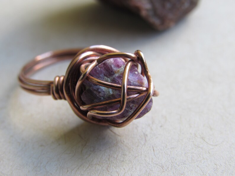 May include: A copper wire wrapped ring with a pink ruby gemstone in the center.