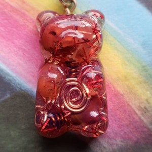 Op de afbeelding: Een ketting met een rode en transparante hars gummy bear hanger met koperen draad details. De hanger is gevormd als een gummy bear en heeft een glanzende, doorschijnende afwerking.