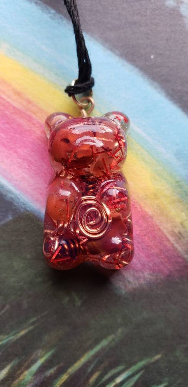 Op de afbeelding: Een ketting met een rode en transparante hars gummy bear hanger met koperen draad details. De hanger is gevormd als een gummy bear en heeft een glanzende, doorschijnende afwerking.