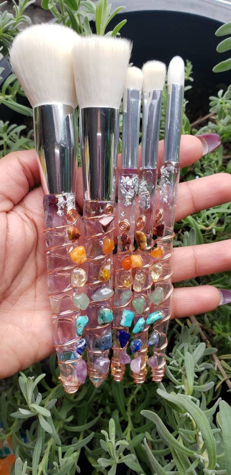 May include: Set of five makeup brushes with clear handles and colourful gemstone accents. The handles are wrapped with copper wire and feature various gemstones, including amethyst, turquoise, and citrine.