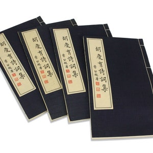 May include: Four black bound books with tan paper spines. The spines have Chinese characters in black ink and a red seal. The text on the spines reads "胡慶育詩詞集".