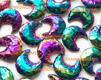Op de afbeelding: Een verzameling van iriserende regenboog-maanstenen cabochons in de vorm van een halve maan. De stenen zijn een mix van paars, groen en blauw.