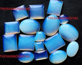 May include: An assortment of polished, opalescent gemstones in various shapes, including squares, rectangles, and ovals. The stones display a gradient of blue and white hues, with the text "THERAINBOWGEMS" visible in red.