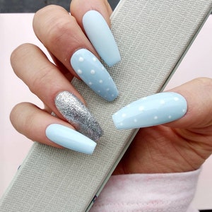 K&ouml;nnte beinhalten: Hellblaue, lange, mandelf&ouml;rmige Kunstn&auml;gel mit wei&szlig;en Punkten und einem Nagel mit silbernem Glitzer.