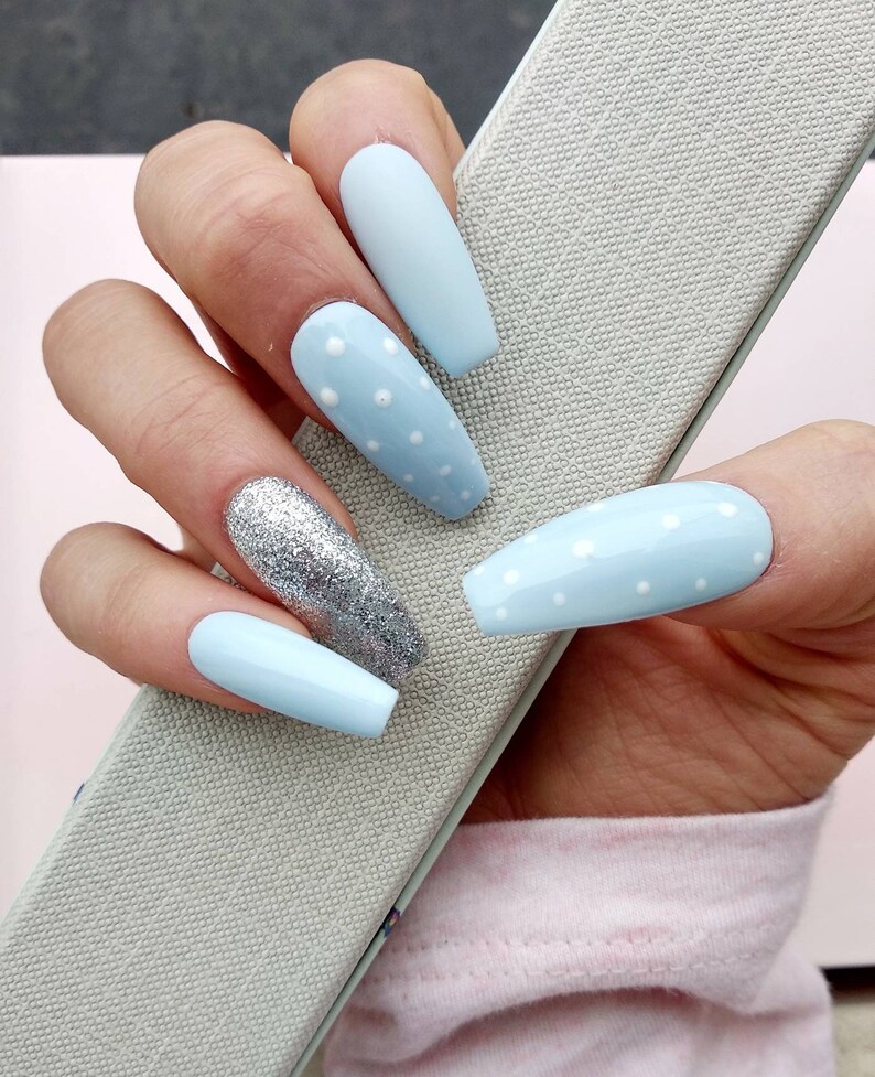 K&ouml;nnte beinhalten: Hellblaue, lange, mandelf&ouml;rmige Kunstn&auml;gel mit wei&szlig;en Punkten und einem Nagel mit silbernem Glitzer.