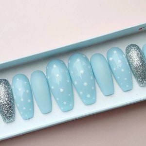K&ouml;nnte beinhalten: Ein Set mit zehn hellblauen Press-on-N&auml;geln mit wei&szlig;en Punkten. Zwei der N&auml;gel sind silberfarben glitzernd.
