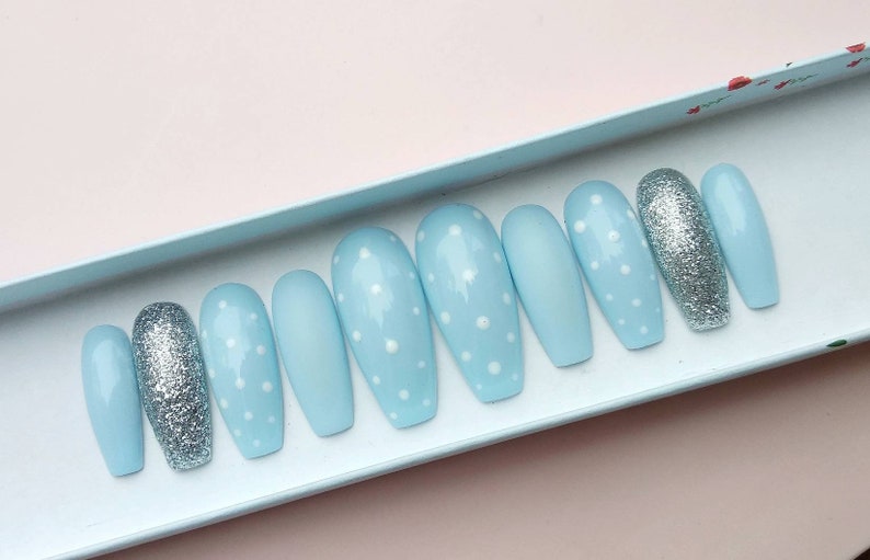 K&ouml;nnte beinhalten: Ein Set mit zehn hellblauen Press-on-N&auml;geln mit wei&szlig;en Punkten. Zwei der N&auml;gel sind silberfarben glitzernd.
