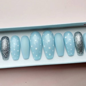 K&ouml;nnte beinhalten: Ein Set mit zehn hellblauen, sargf&ouml;rmigen Press-on-N&auml;geln mit wei&szlig;en Punkten. Ein Nagel ist silberfarben glitzernd.