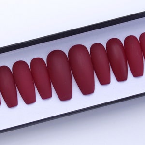 May include: A set of ten burgundy matte press-on nails in a coffin shape.