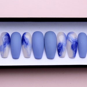 Puede incluir: Un juego de diez u&ntilde;as artificiales en forma de ata&uacute;d. Las u&ntilde;as alternan entre azul mate s&oacute;lido y un dise&ntilde;o de remolinos azules sobre una base blanca. Las u&ntilde;as se exhiben en una caja negra.