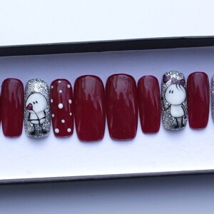 May include: Set of ten burgundy press-on nails with silver glitter and a design of two cartoon figures holding hearts.