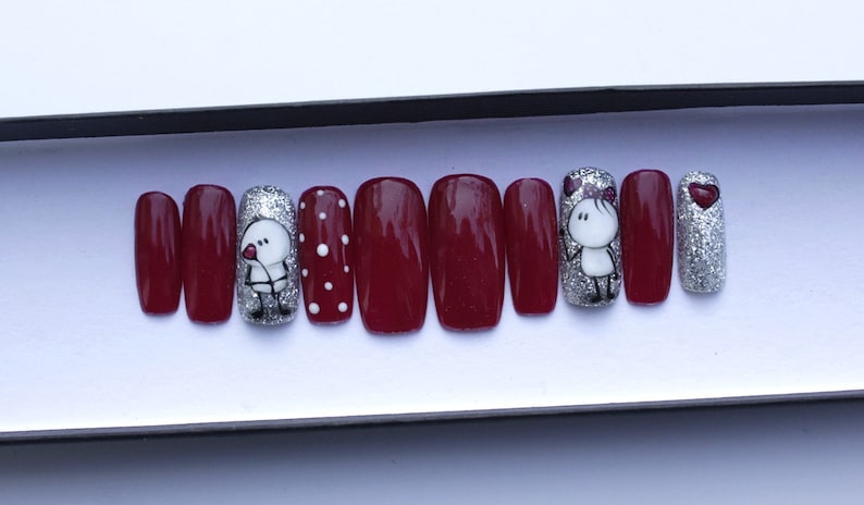 May include: Set of ten burgundy press-on nails with silver glitter and a design of two cartoon figures holding hearts.